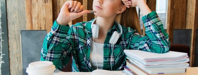A girl sitting at a table with her head up and holding a pencil.
