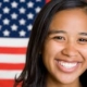 A woman smiles in front of an american flag.